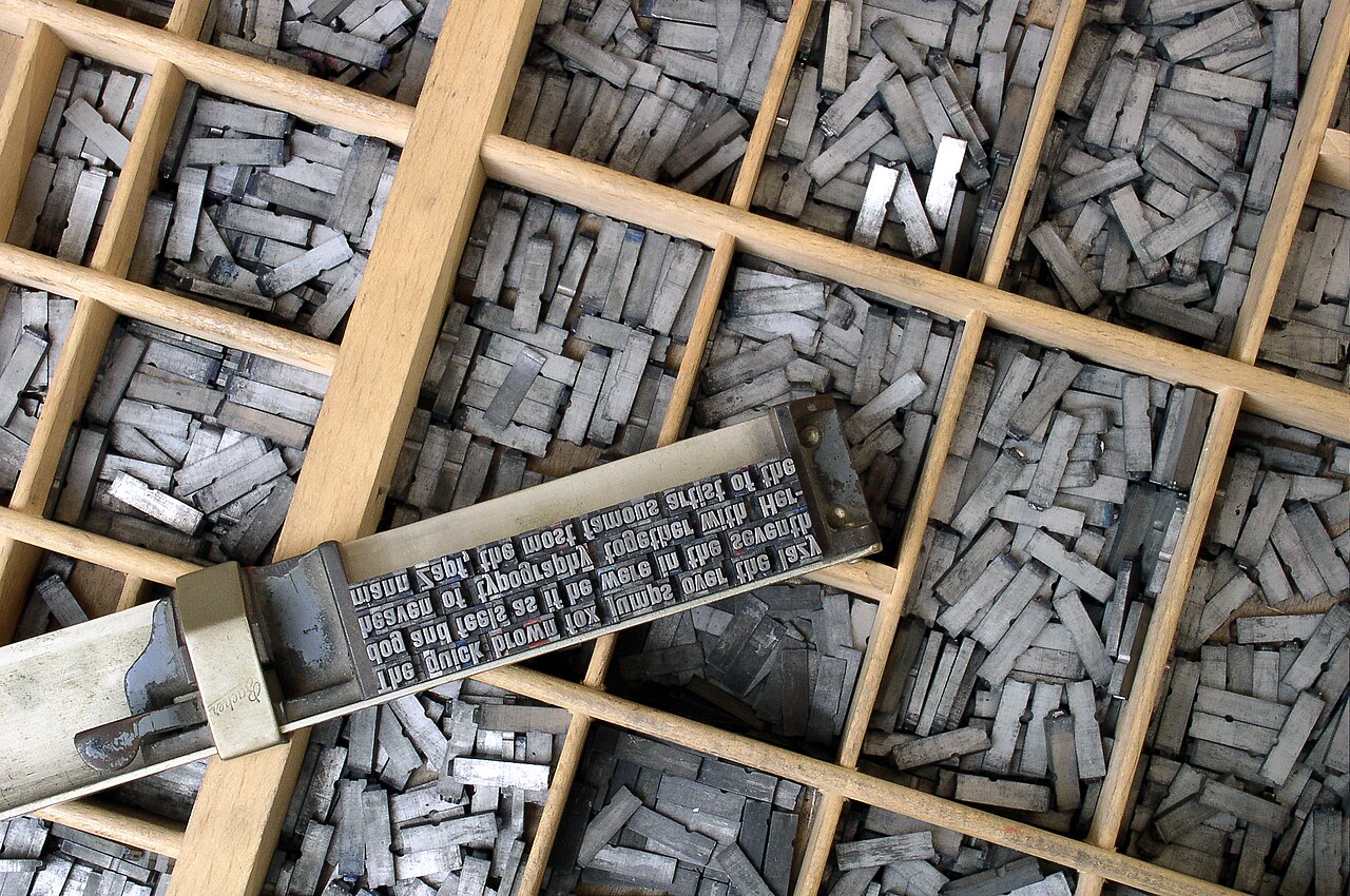 Drawers of metal letterpress type with a composing stick holding set lines of text.