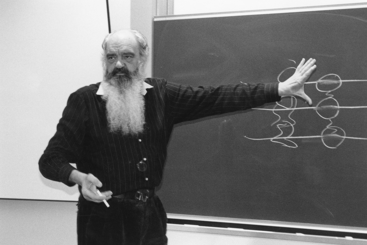 Stafford Beer, white bearded, pointing at a diagram on a blackboard during a lecture.