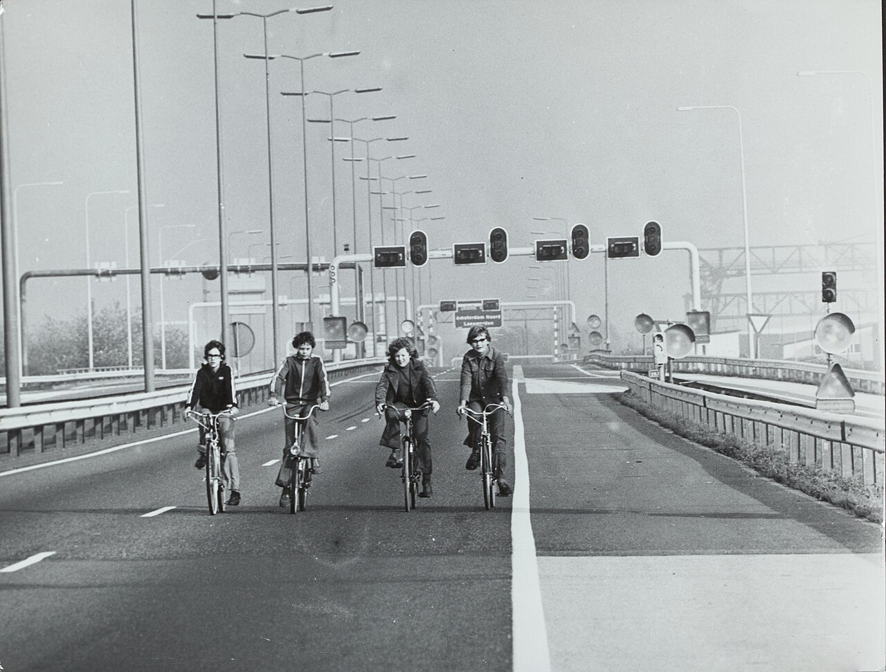 Four young people cycling side by side along an empty motorway in Amsterdam on a car-free Sunday, January 1974.