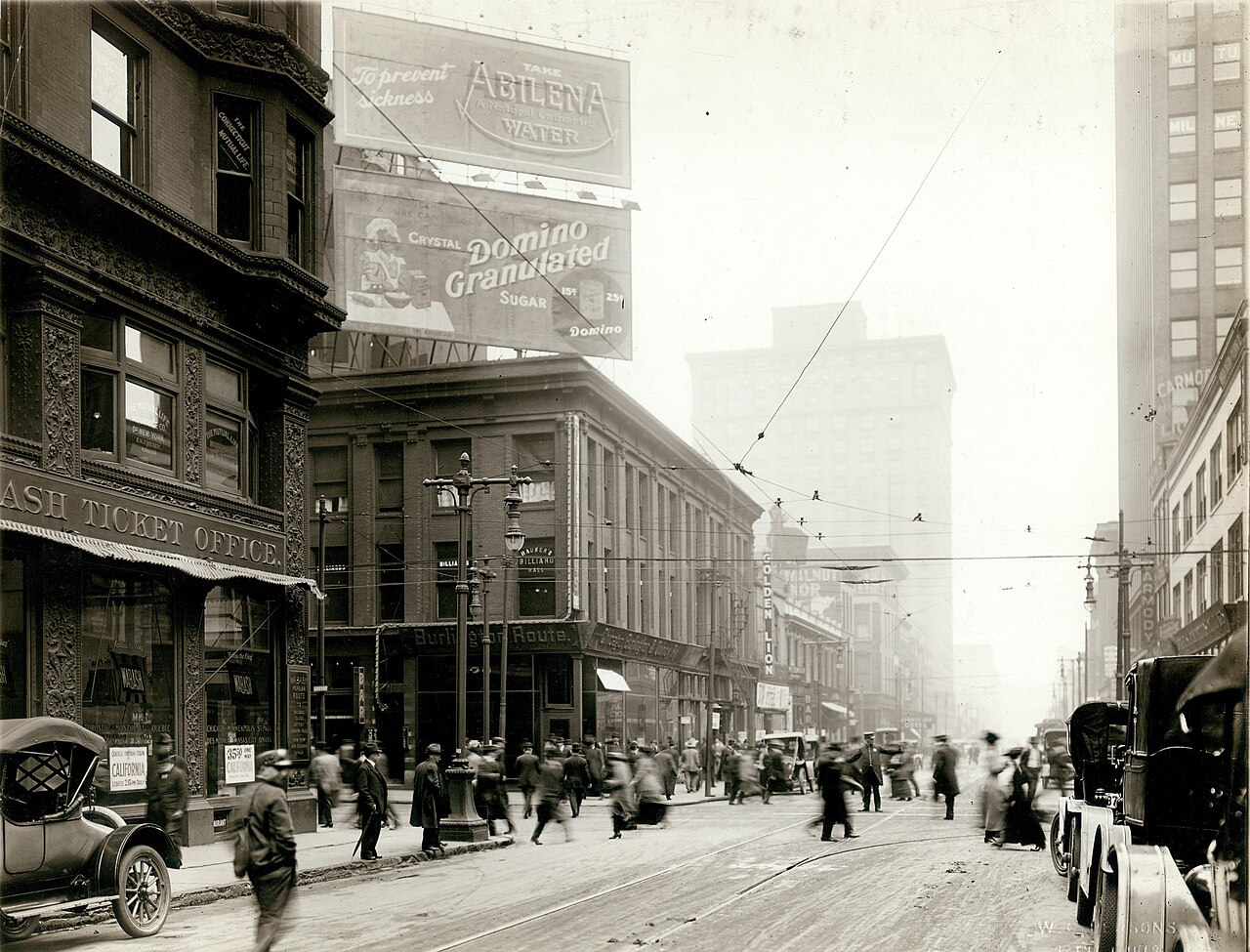 Pedestrians walk across a St. Louis street among early cars and streetcar tracks, about 1915.