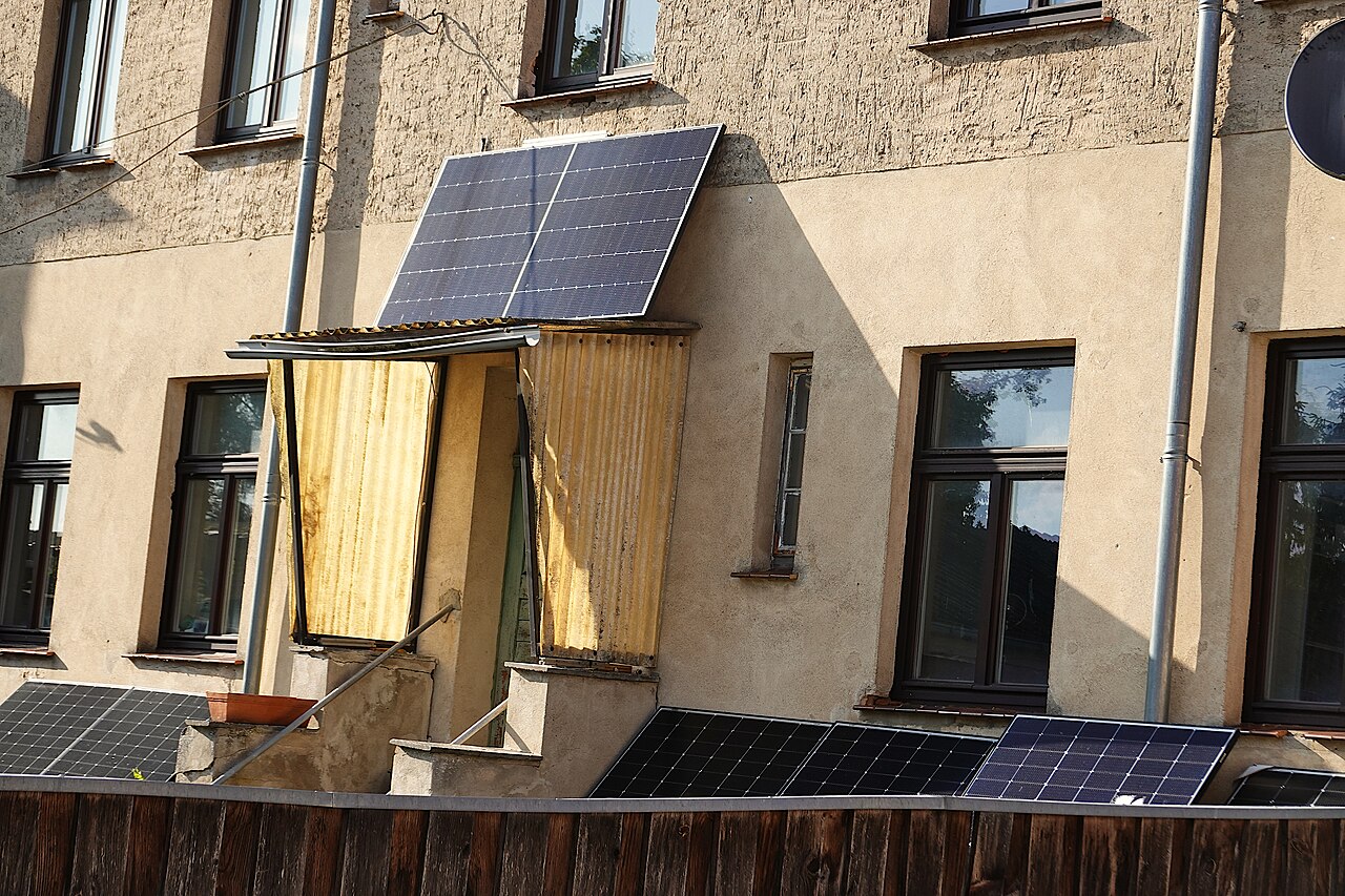 Small solar panels mounted over a doorway and along a fence in front of an old house.