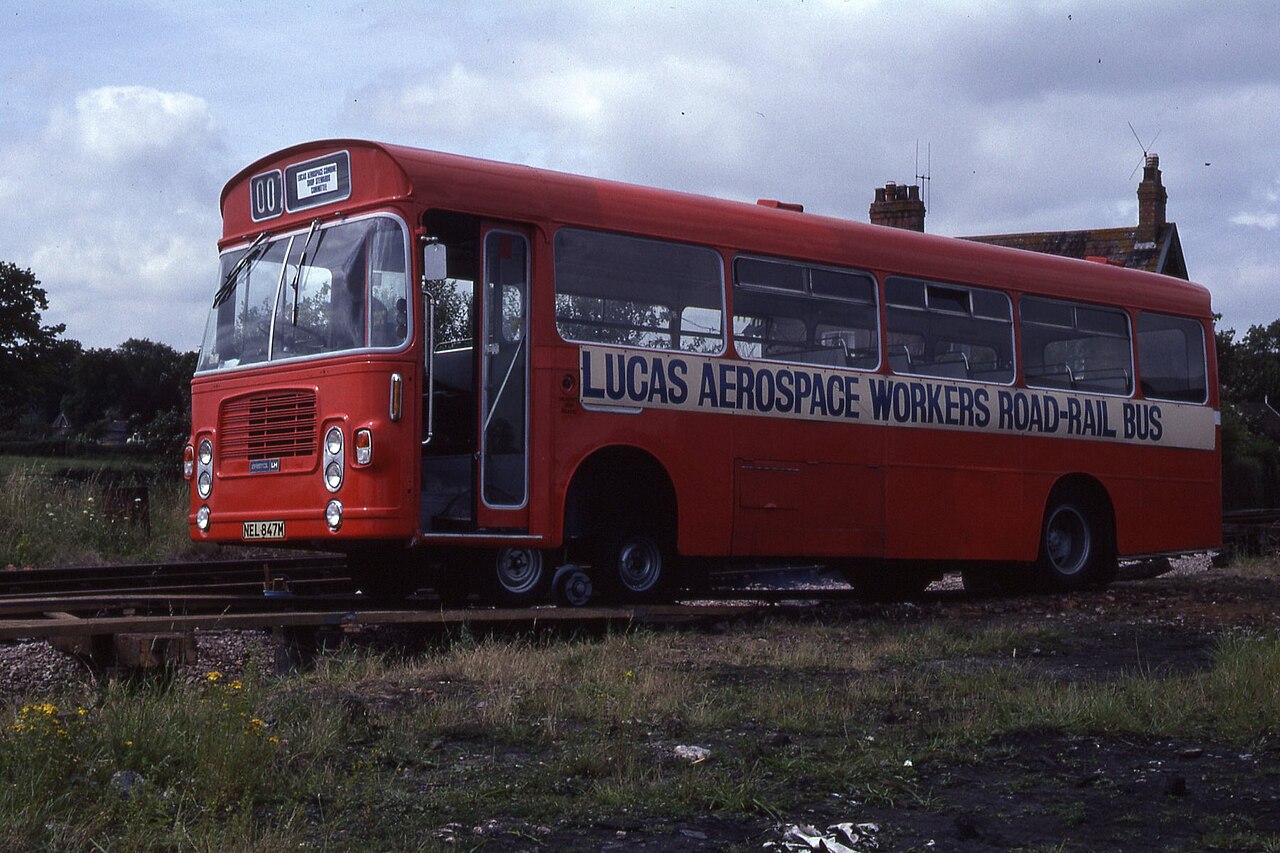 A red bus marked 'Lucas Aerospace Workers Road-Rail Bus' standing on railway track in 1980.