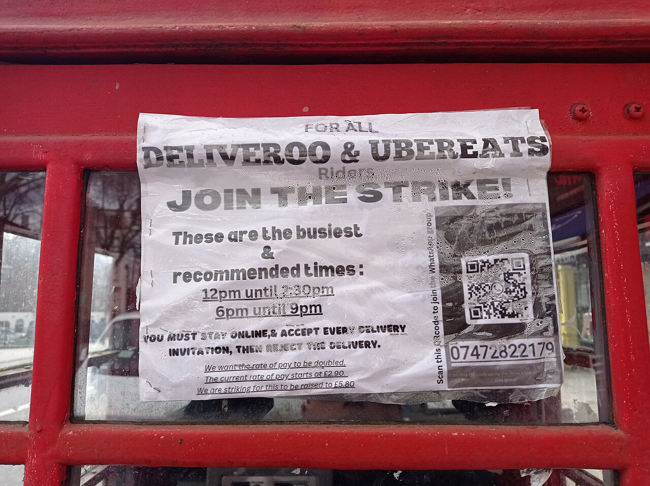 A paper notice on a red London phone box calling Deliveroo and Uber Eats riders to strike.